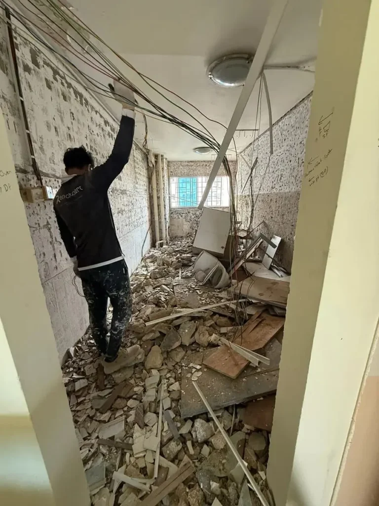 Construction worker organizing overhead wiring in a room with hacked tile floors during a residential renovation in Singapore.