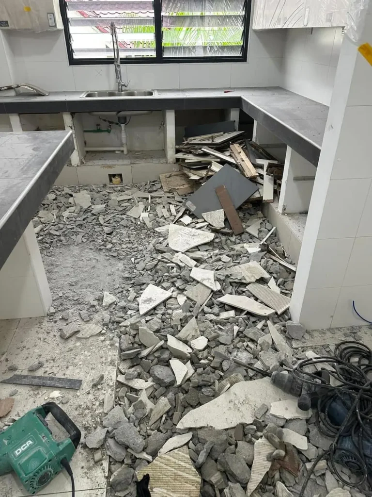 Kitchen floor tiles hacked and removed with concrete rubble and power tools during residential kitchen demolition in Singapore.