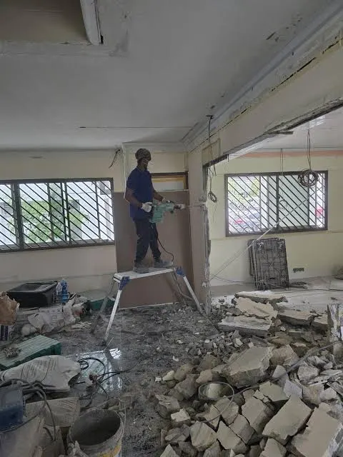 Construction worker standing on a work platform using a jackhammer for professional wall hacking services in a Singapore residential renovation.